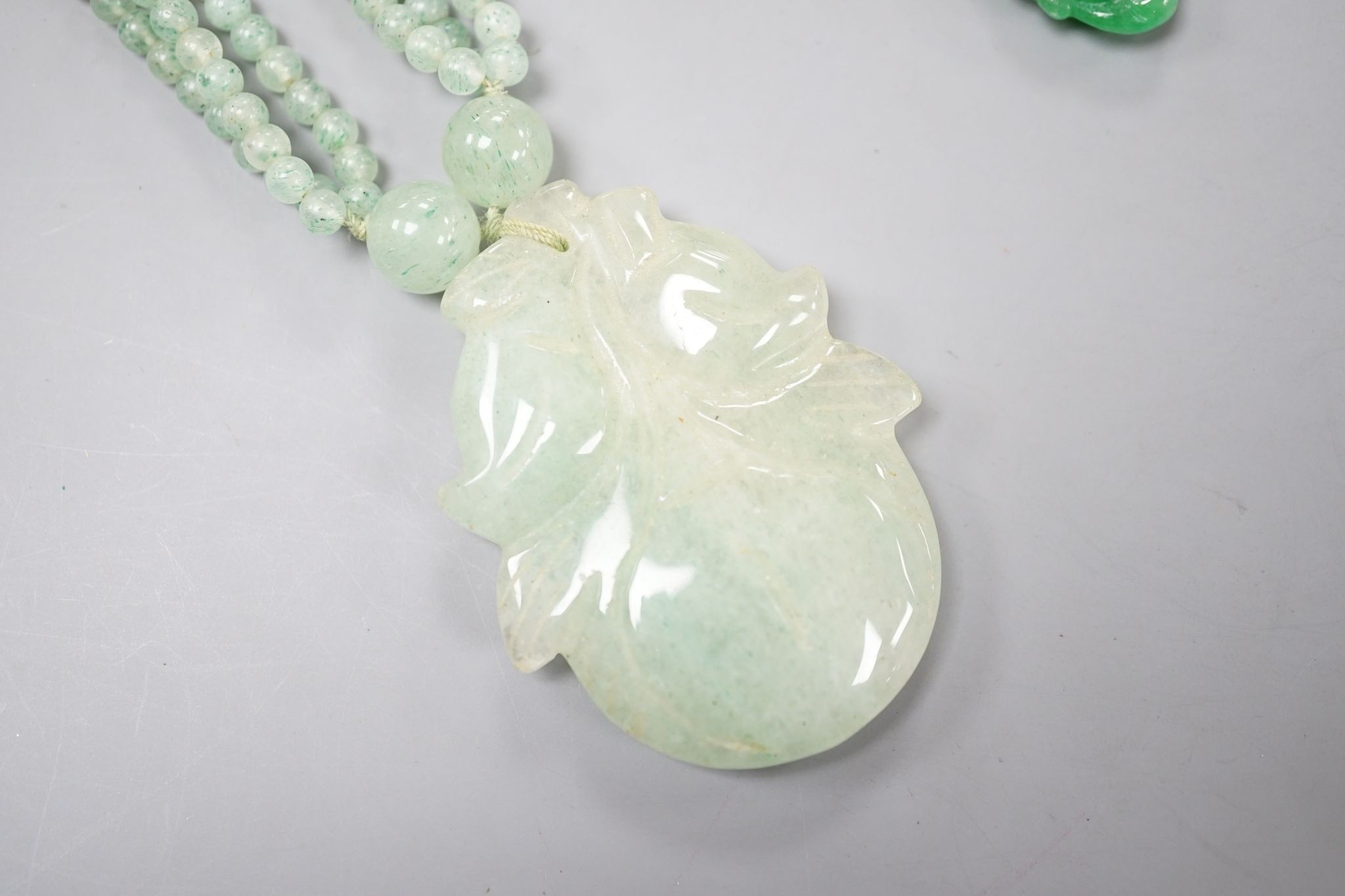 A carved jade pendant, 53mm on a quartz bead necklace, one other jade pendant and a jade, paste and gilt metal ring.